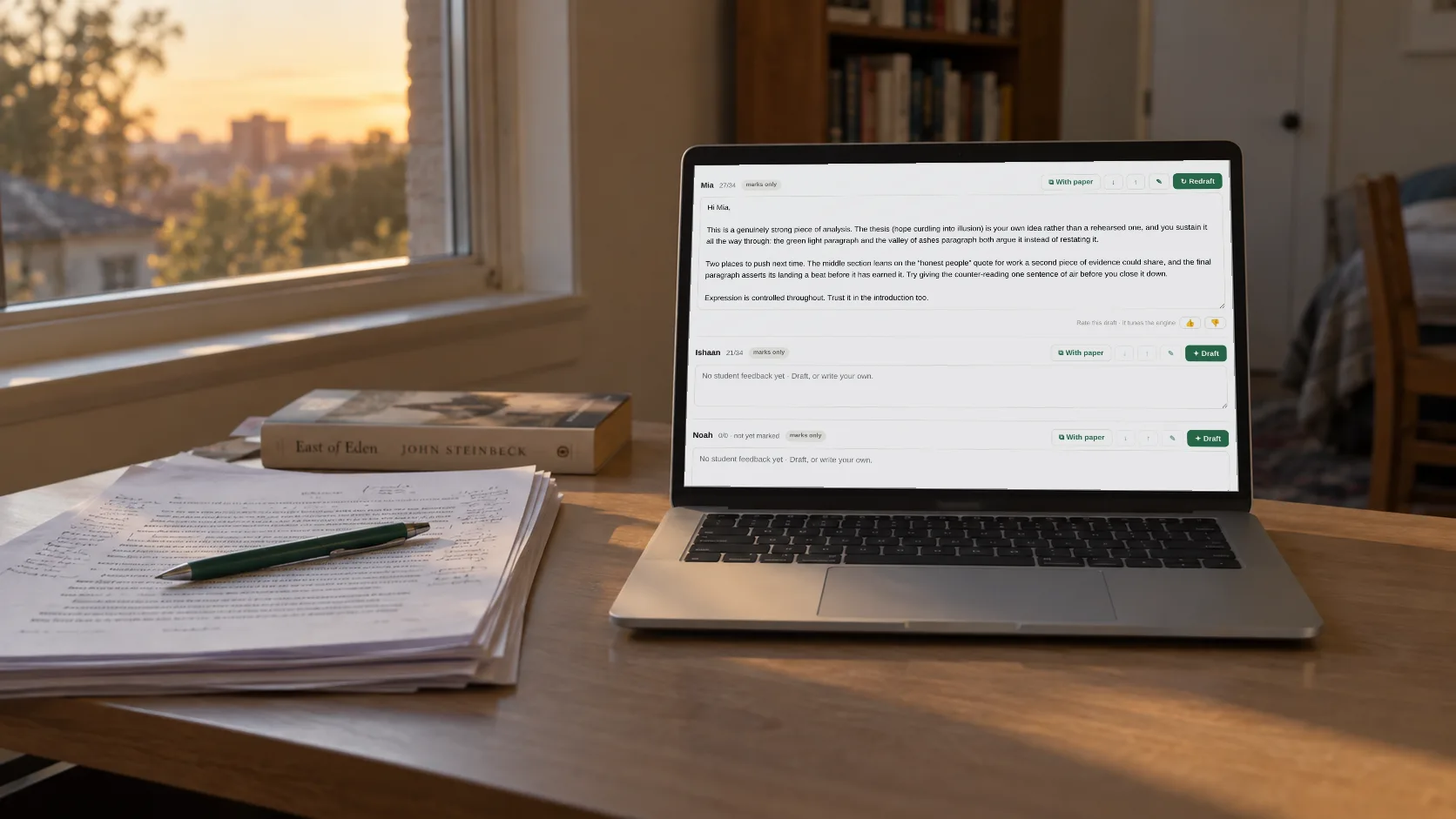 Essay feedback on a laptop beside a pile of essays